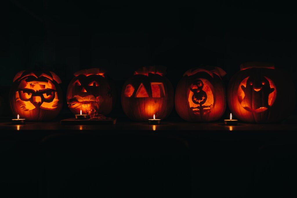 Five carved pumpkins with candles illuminating them in the dark